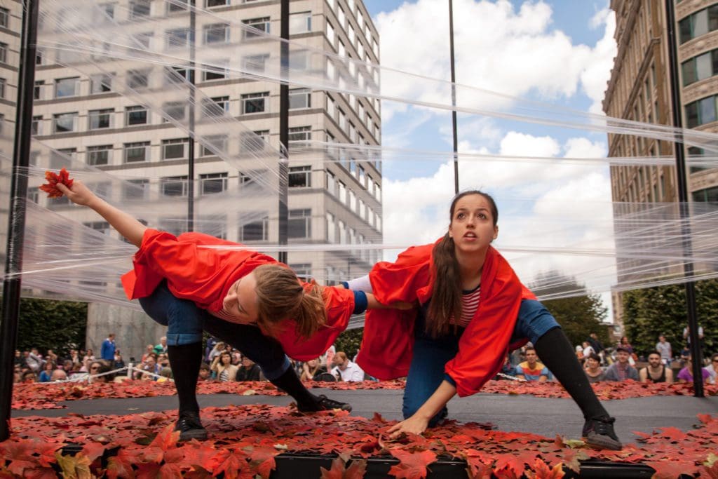 Two women in red cloaks crouch and look up to the sky
