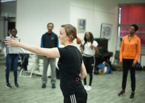 A woman stands in front of some young people and points towards one of them.