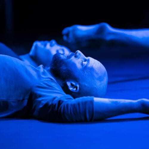A man lies on the floor bathed in blue light.
