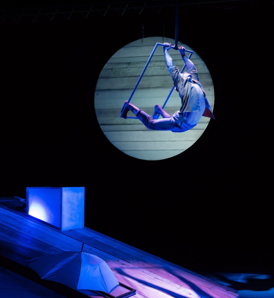 A performer swings on a trapeze high above a stage