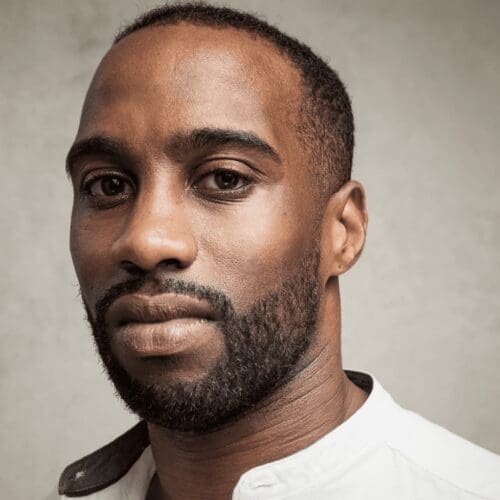 Close up headshot of a man with short hair and a beard wearing a white shirt.