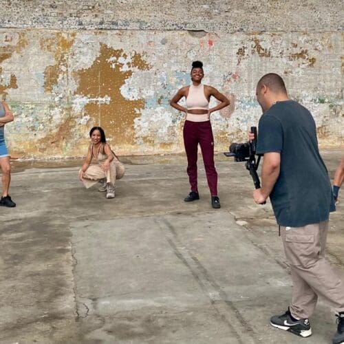 A group of people stand in front of a brick wall and pose as a photographer takes a photo of them,