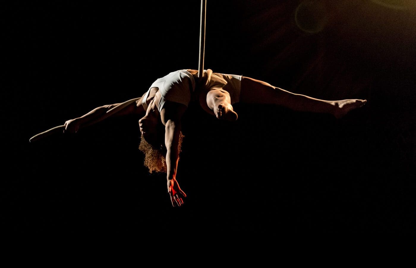 An Upswing aerialist suspended by aerial rope upside down in a black room