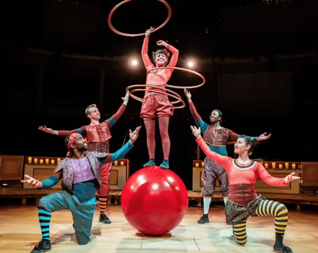 A group of circus performers performing on a blow up ball with hula hoops in a circus show