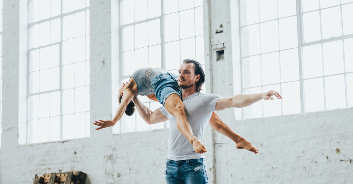 A female acrobat balances backwards across the shoulders of a male acrobat base